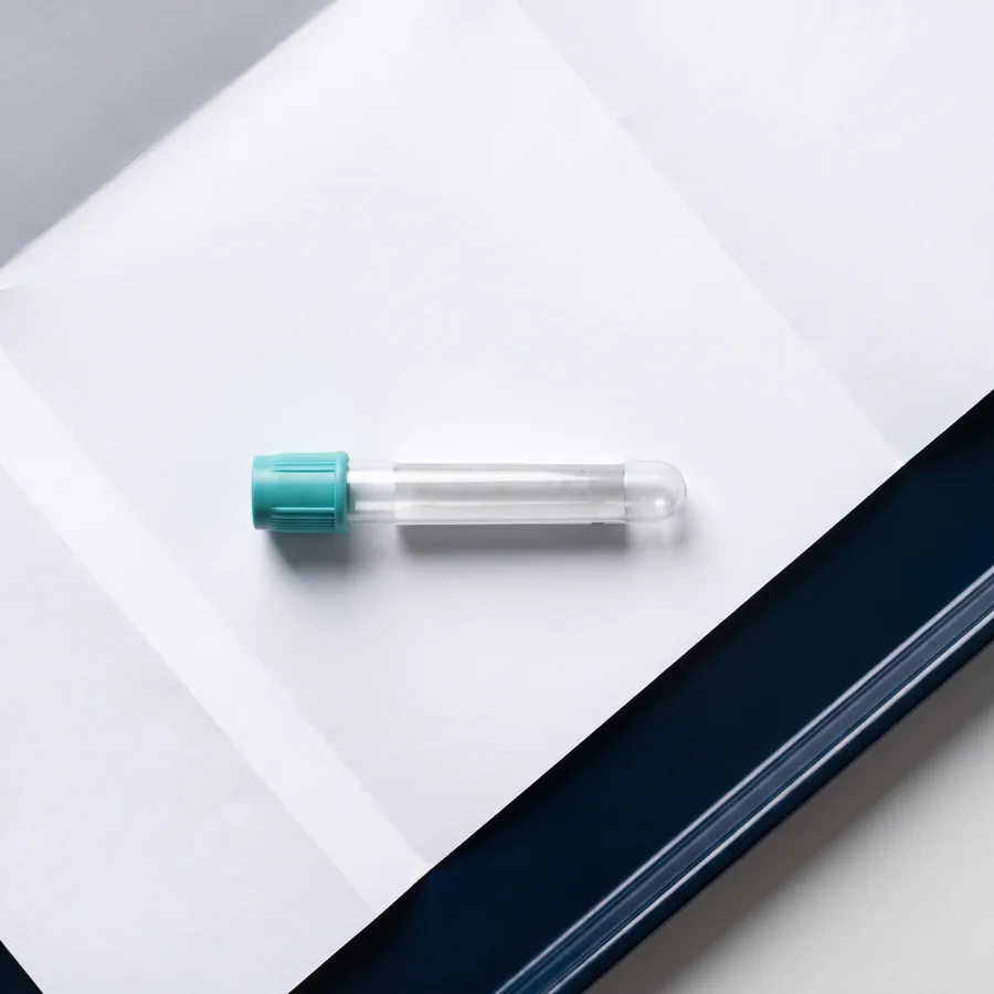 A blood-draw tube with a teal cap resting on a printed lab requisition.